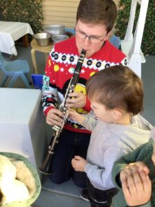 A musician playing some flute and showing a litlle toddler boy how it works.